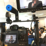 Eine Filmkamera von Sony auf einem Gestell mit einem externen Monitor filmt eine blonde Frau, die ein Mikrofon in der Hand hat. EB-Team in Aschaffenburg
